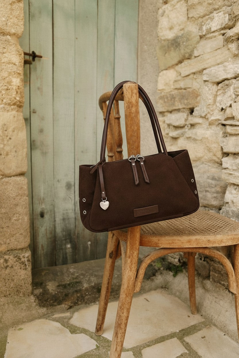 Urban Originals USA Please Stay chocolate brown suede crossbody bag with silver hardware hanging on a wooden chair