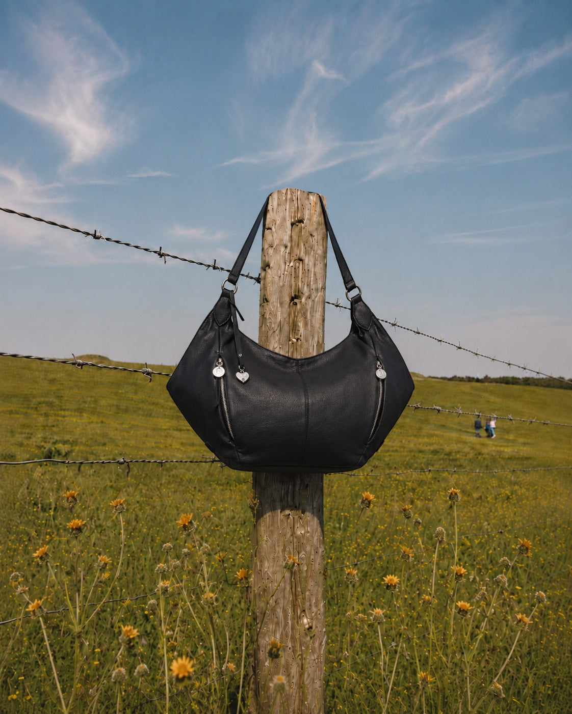 Urban Originals USA Destiny black vegan leather hobo bag with winged silhouette hanging on a wooden fence post